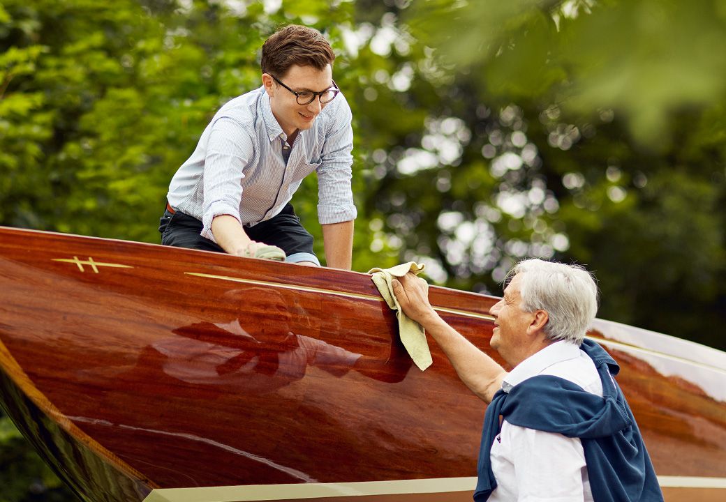 Symbolbild: Familie poliert gemeinsam ein Boot – Sinnbild für Sorgfalt, Zusammenhalt und den generationenübergreifenden Erhalt von Vermögen